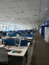 Open-plan office with rows of desks, computers, and employees working in a modern corporate workspace.