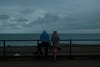 A couple staring at the sea leaning on a guard rail.