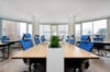 Empty open-plan office with a long shared desk, blue mesh chairs and floor-to-ceiling windows overlooking a city