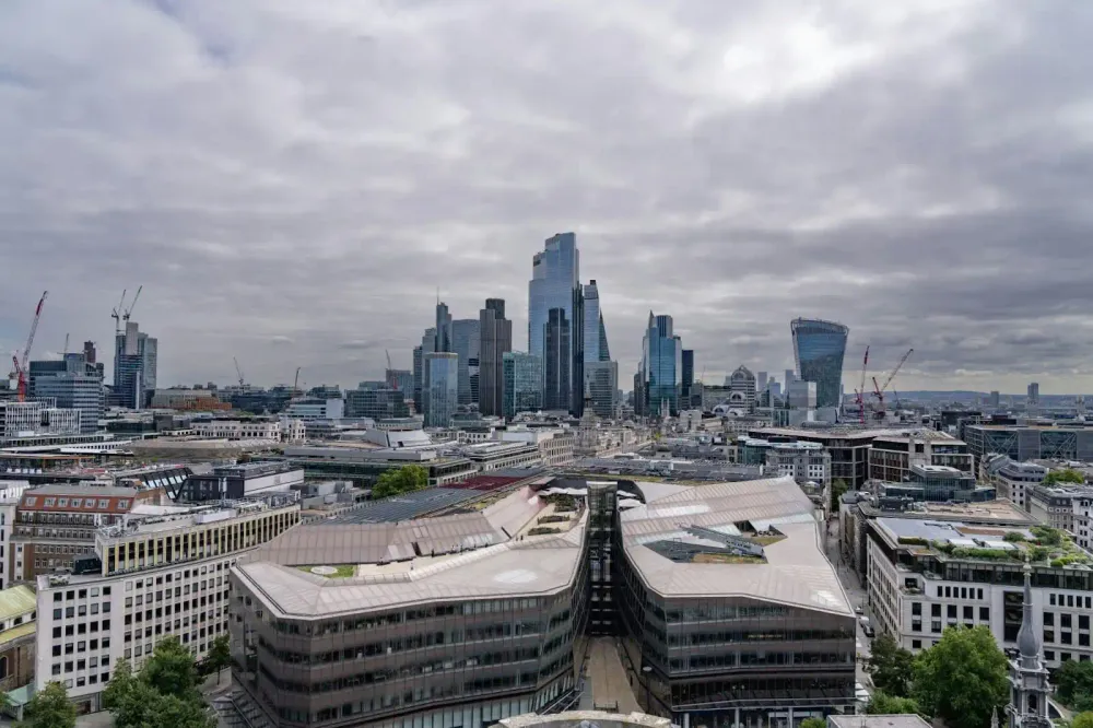 A panoramic view of London's skyline featuring modern skyscrapers, construction cranes, and a cloudy sky.