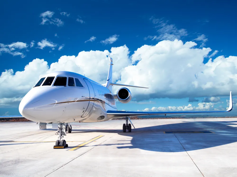 A sleek white private jet parked on a runway under a bright blue sky with fluffy clouds, showcasing its elegant design.