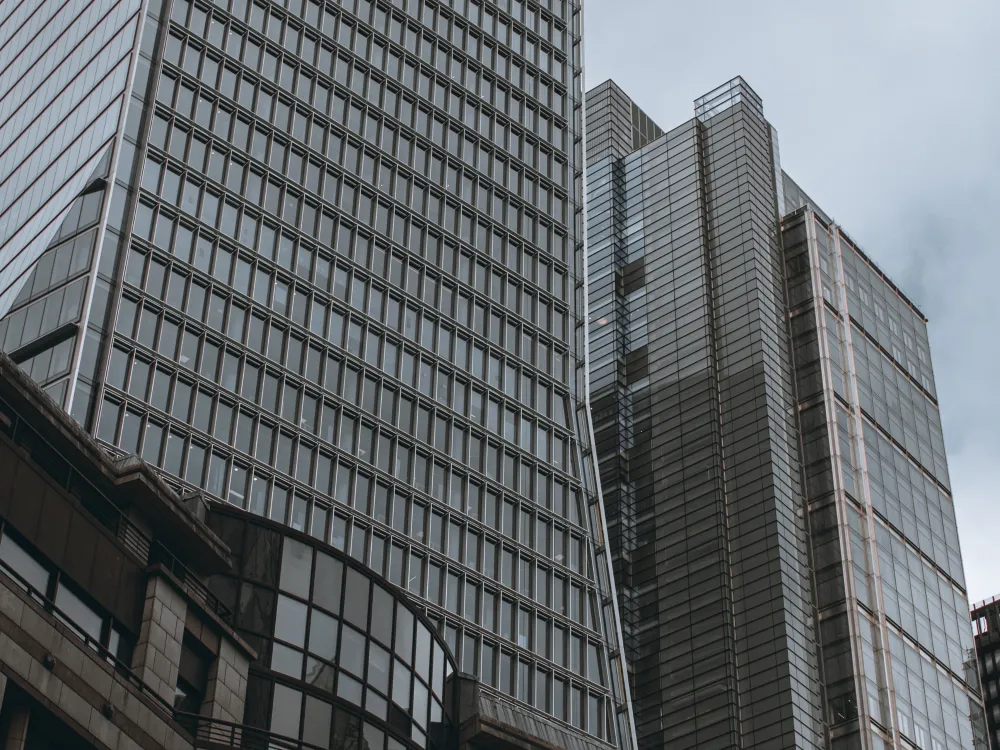 A view of modern skyscrapers from below, showcasing glass facades and geometric designs against a cloudy sky.
