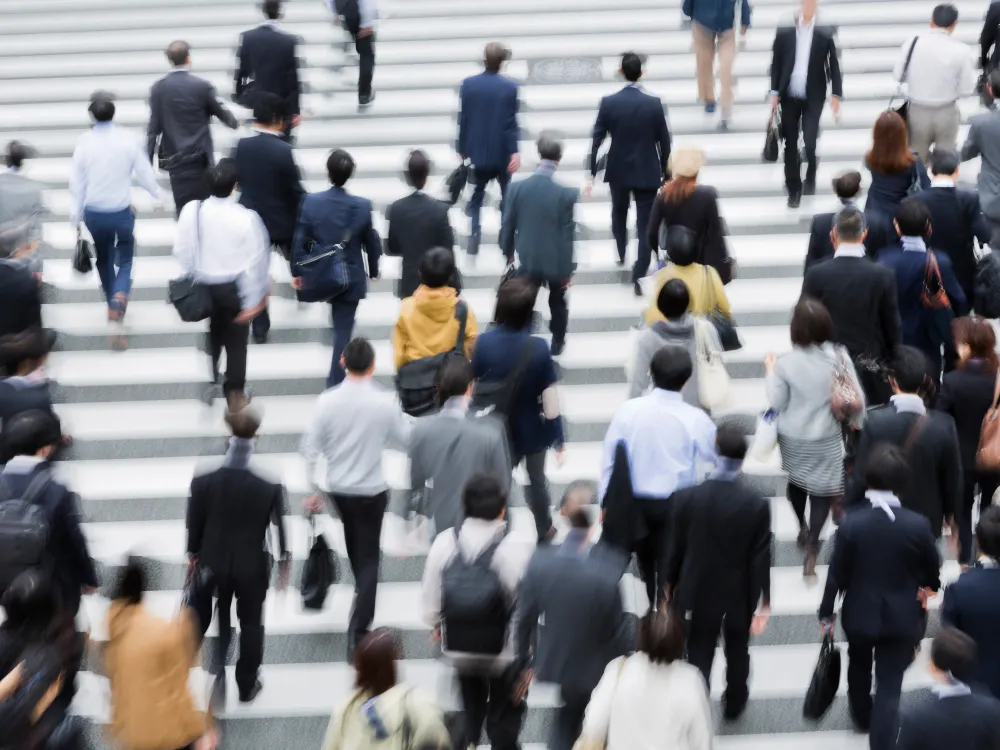 A crowd of people, mostly in business attire, walking across a large crosswalk in an urban setting.