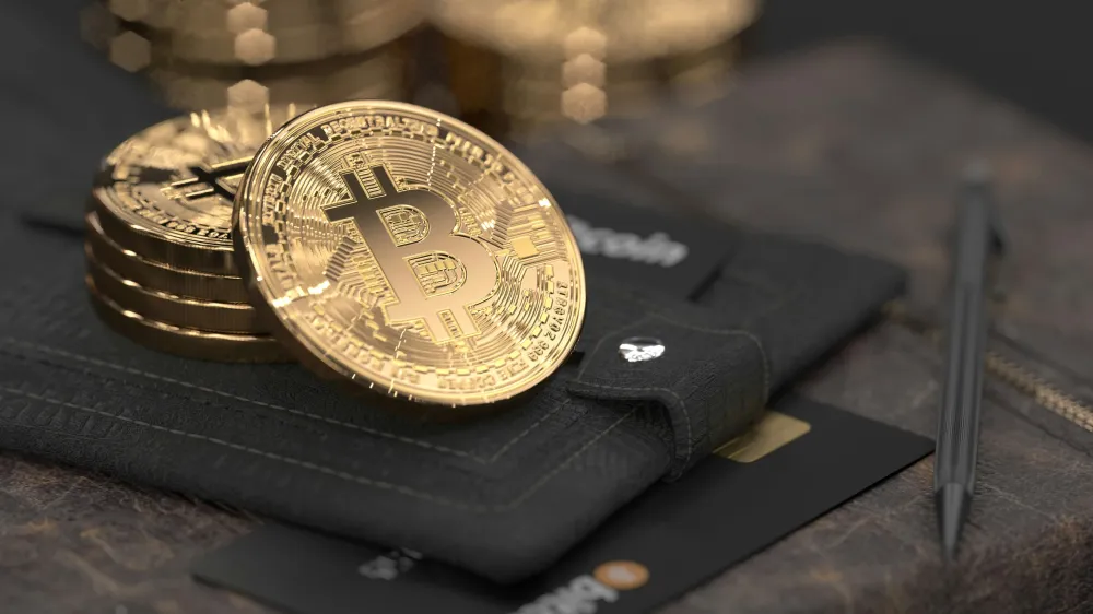 Gold Bitcoin coins resting on a black wallet with a credit card partially visible underneath, symbolizing digital assets used in corporate treasury or financial strategy.