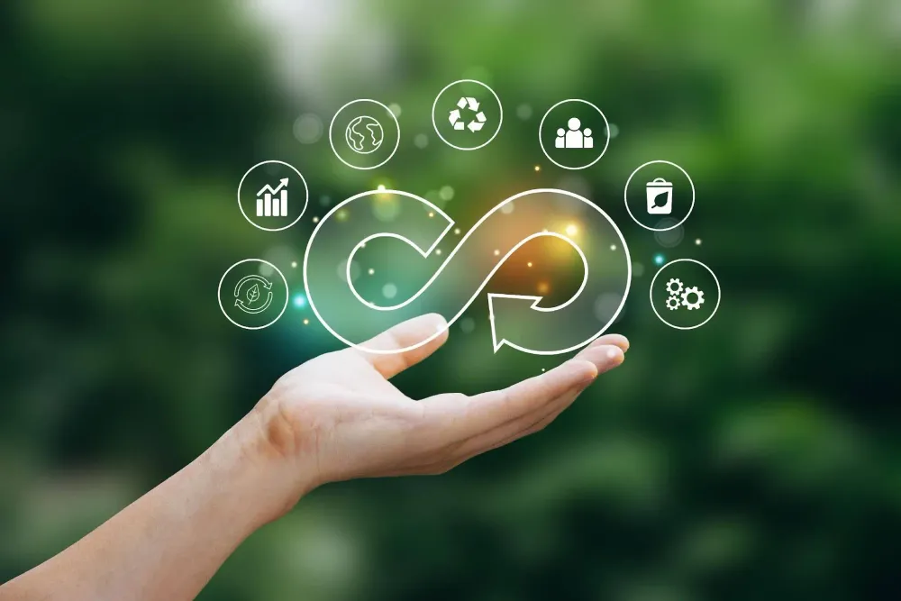 Hand holding a glowing circular economy symbol with recycling and sustainability icons against a green blurred background.