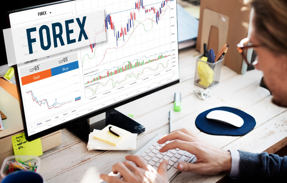 Trader at a desk working on a forex platform showing candlestick charts and buy and sell buttons