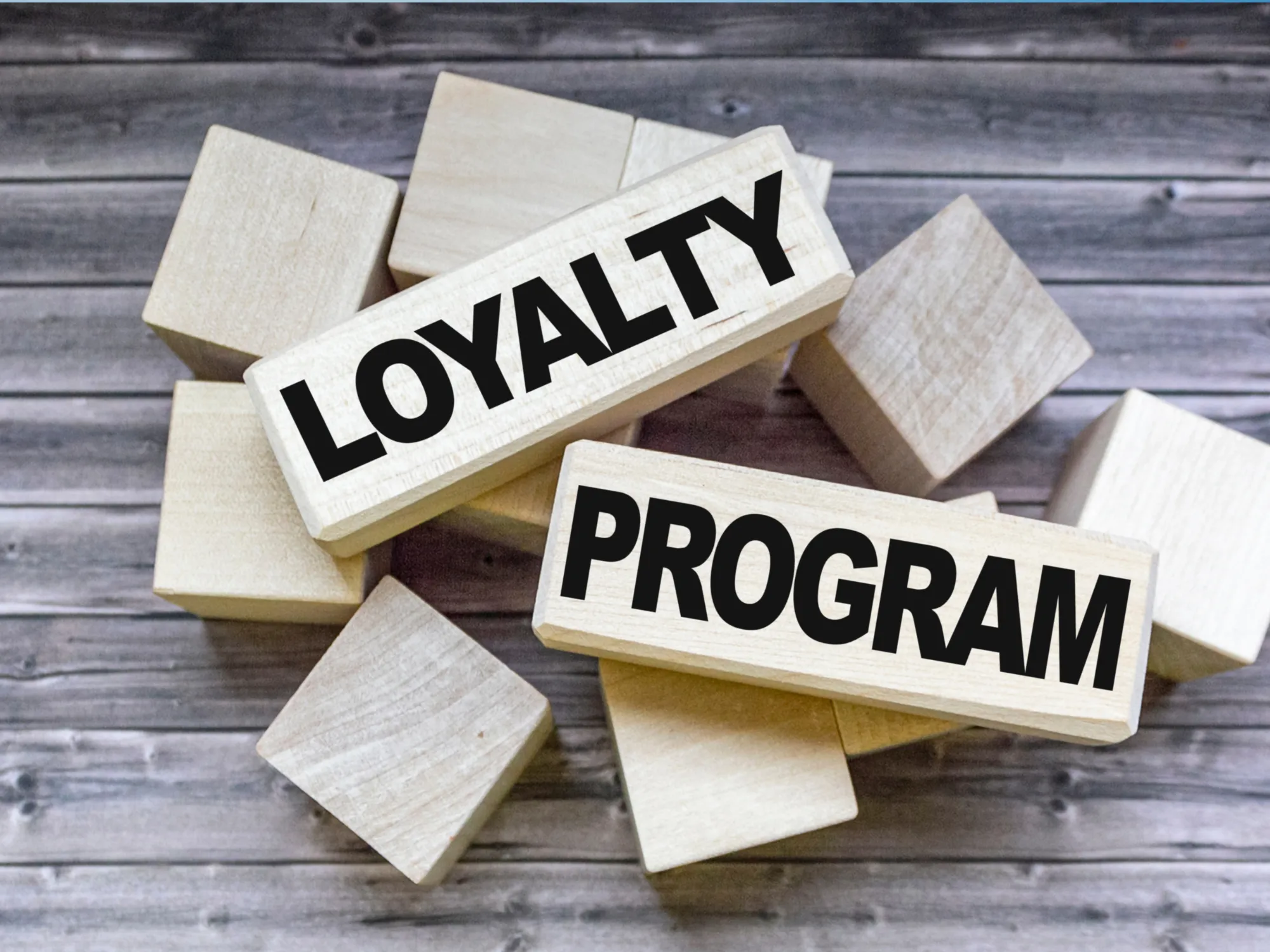 Two wooden blocks labeled "LOYALTY" and "PROGRAM" are placed atop a scattering of smaller wooden cubes on a wooden background.