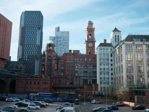 Cityscape featuring a mix of historic and modern architecture, including a red brick building with a tower and clock amidst tall glass structures.