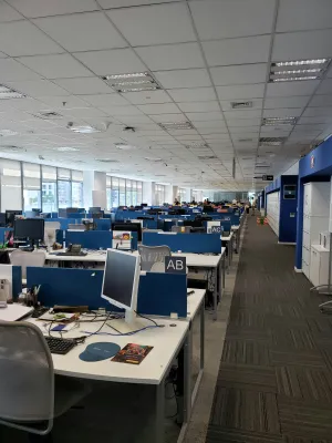Open-plan office with rows of desks, computers, and employees working in a modern corporate workspace.
