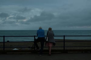 A couple staring at the sea leaning on a guard rail.