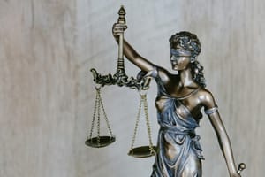 Bronze statue of Lady Justice wearing a blindfold and holding balanced scales, symbolizing fairness, impartiality, and the legal system, against a neutral background.