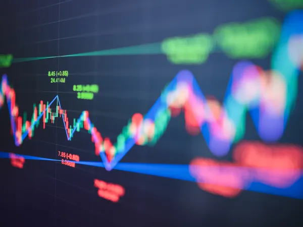 Colorful stock market graph with sharp ups and downs on a dark background, featuring green, red, and blue lines with numerical data, conveying volatility.