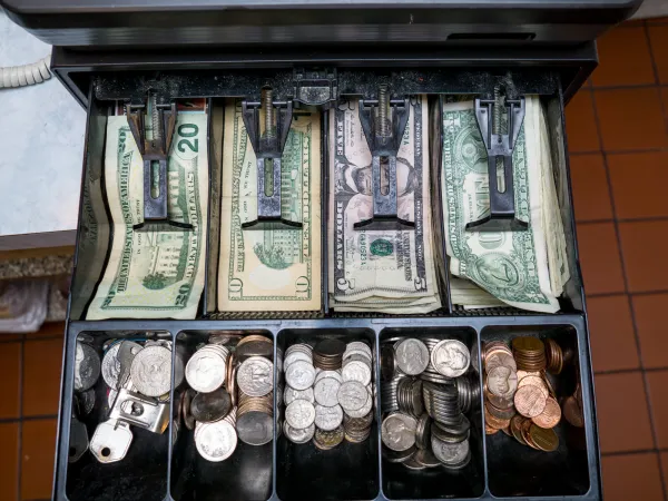 An opened cash register filled with USD currency.