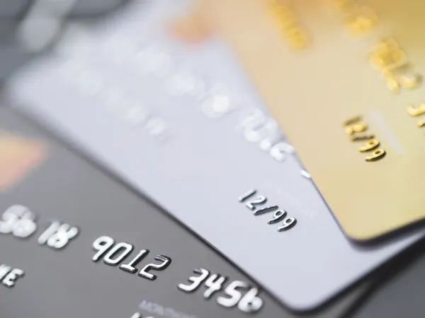 Close-up of three credit cards in varying colors, displaying embossed numbers and expiration dates, on a blurred background.