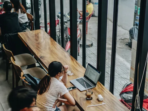 Woman working on a laptop in a café by a window, illustrating remote work and digital nomad lifestyle.