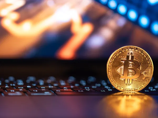 Bitcoin coin on a laptop keyboard with a rising cryptocurrency price chart in the background.