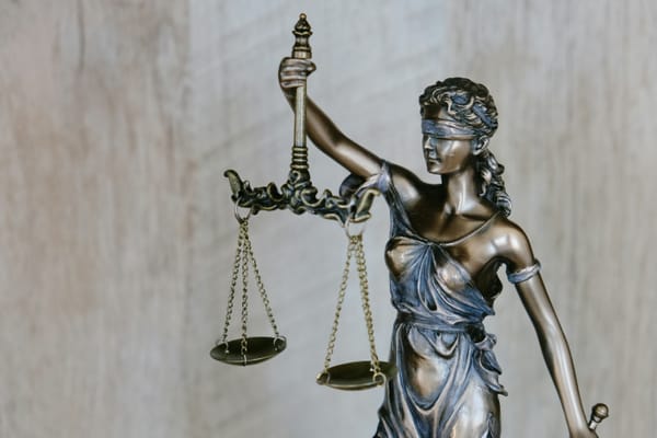 Bronze statue of Lady Justice wearing a blindfold and holding balanced scales, symbolizing fairness, impartiality, and the legal system, against a neutral background.